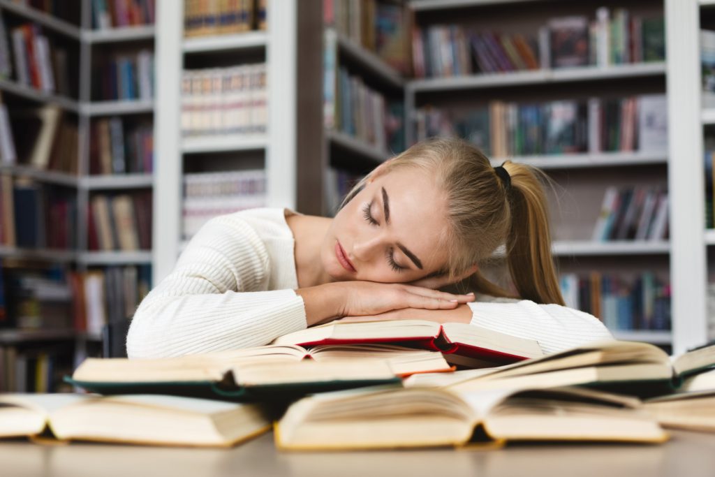 Young blonde girl having nap while studying at library